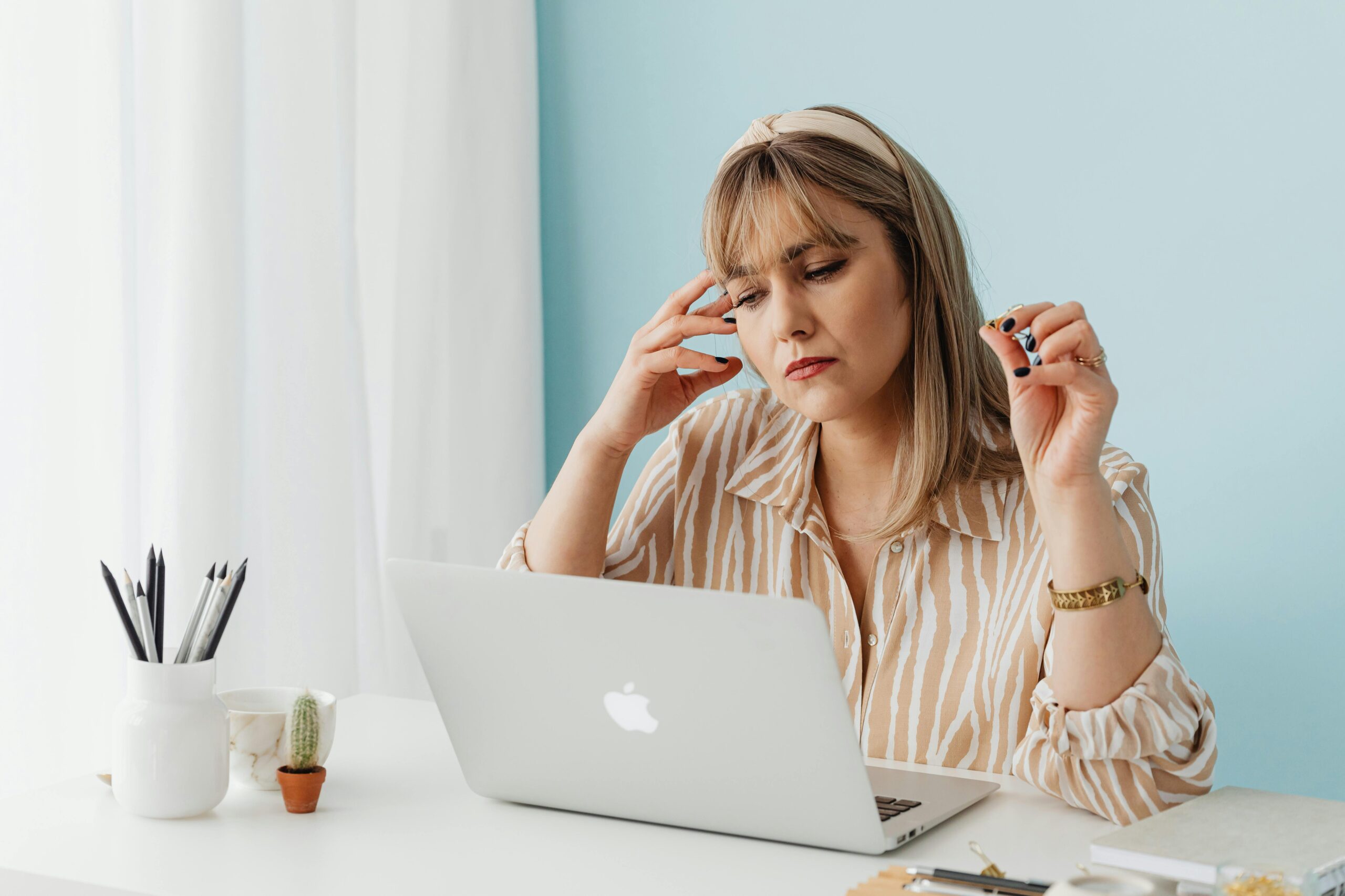 A woman appearing stressed while working on a laptop at a home office setting.